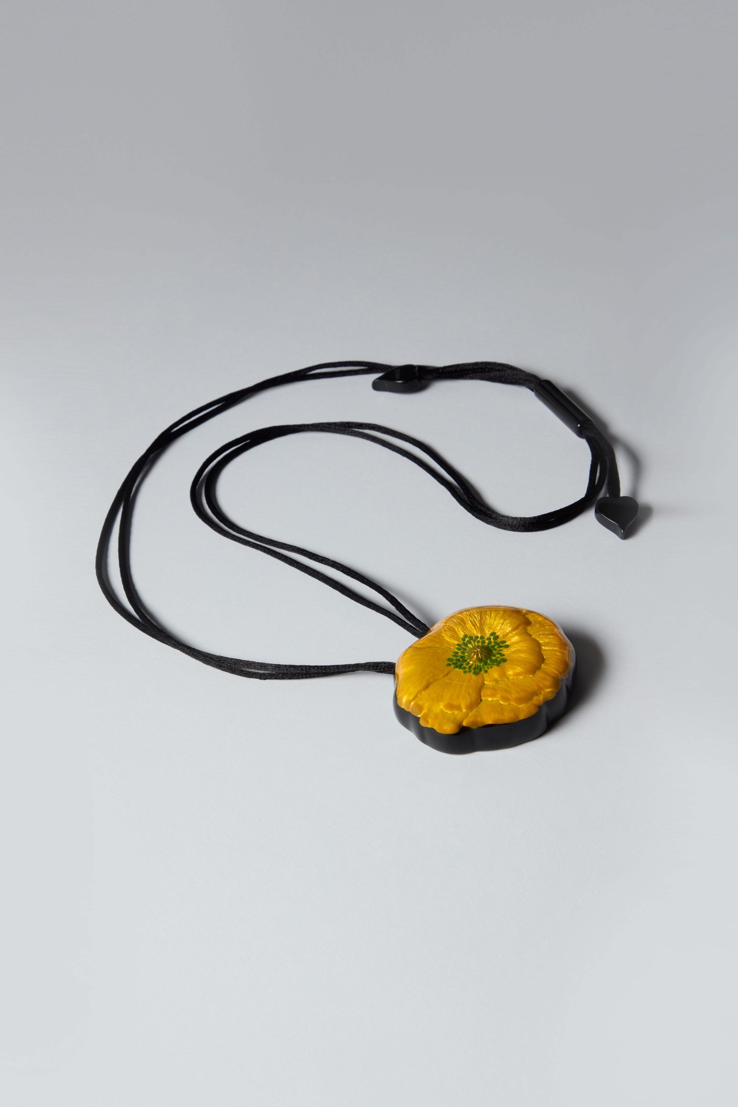 Introducing the Garland Pendant: a handcrafted, yellow flower-shaped masterpiece on an adjustable black cord necklace, strikingly set against a gray background.
