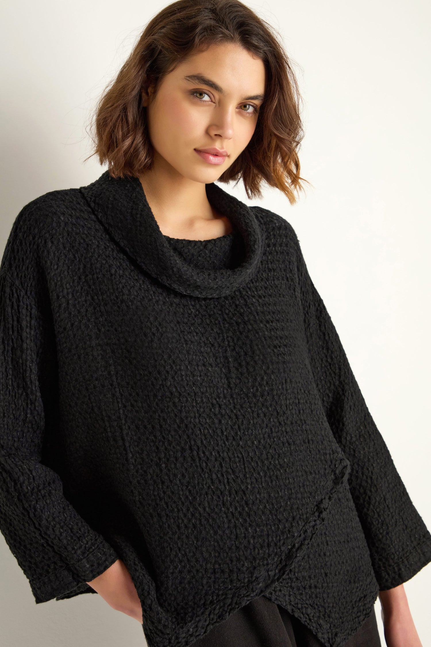 A person with short brown hair is wearing a relaxed fit black Waffle Linen Boxy Cowl Neck Top and black pants, standing against a plain light background.