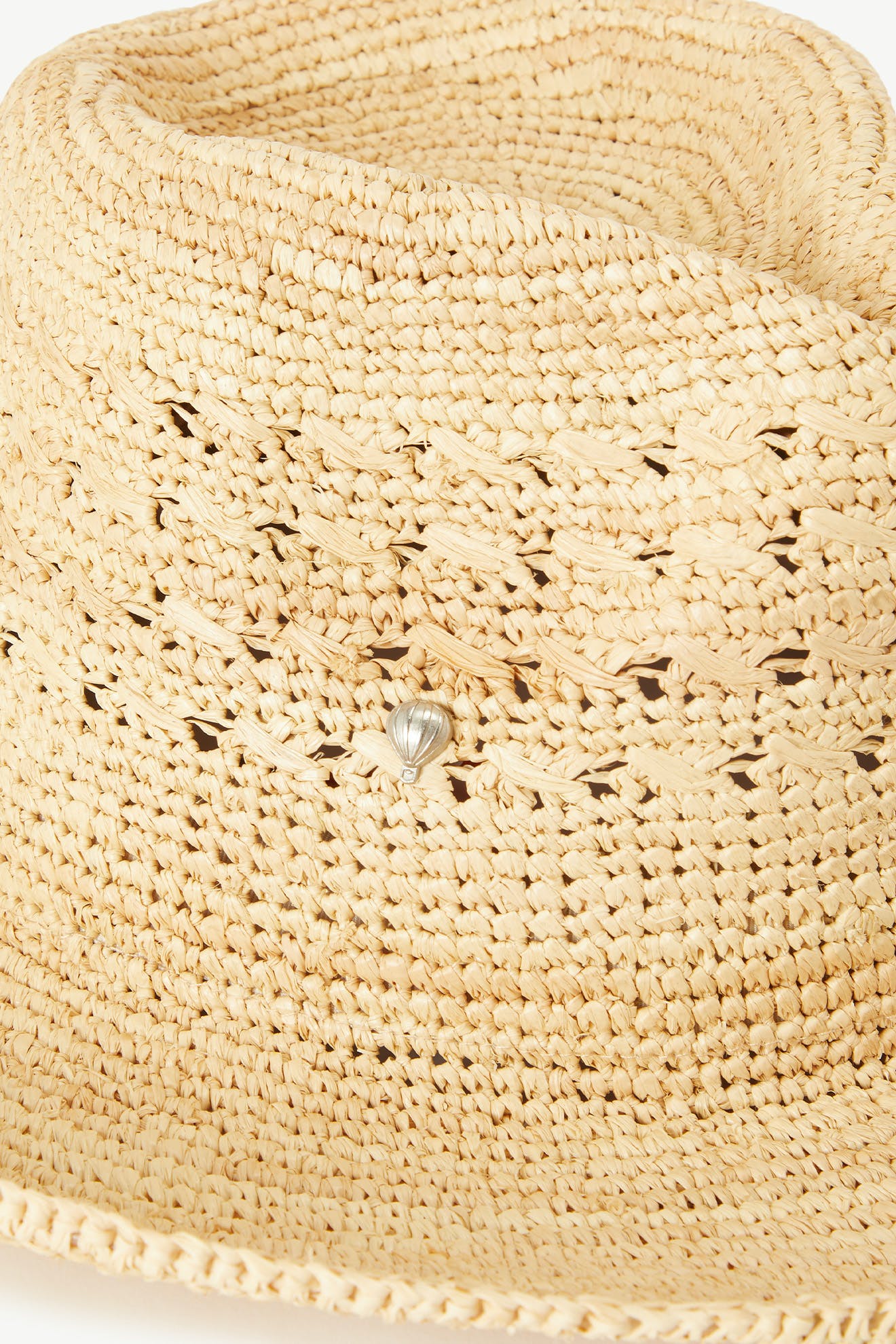 Close-up of the Chapeau Westosia, a lightweight summer hat with a fine weave and a small silver seashell charm on the band.