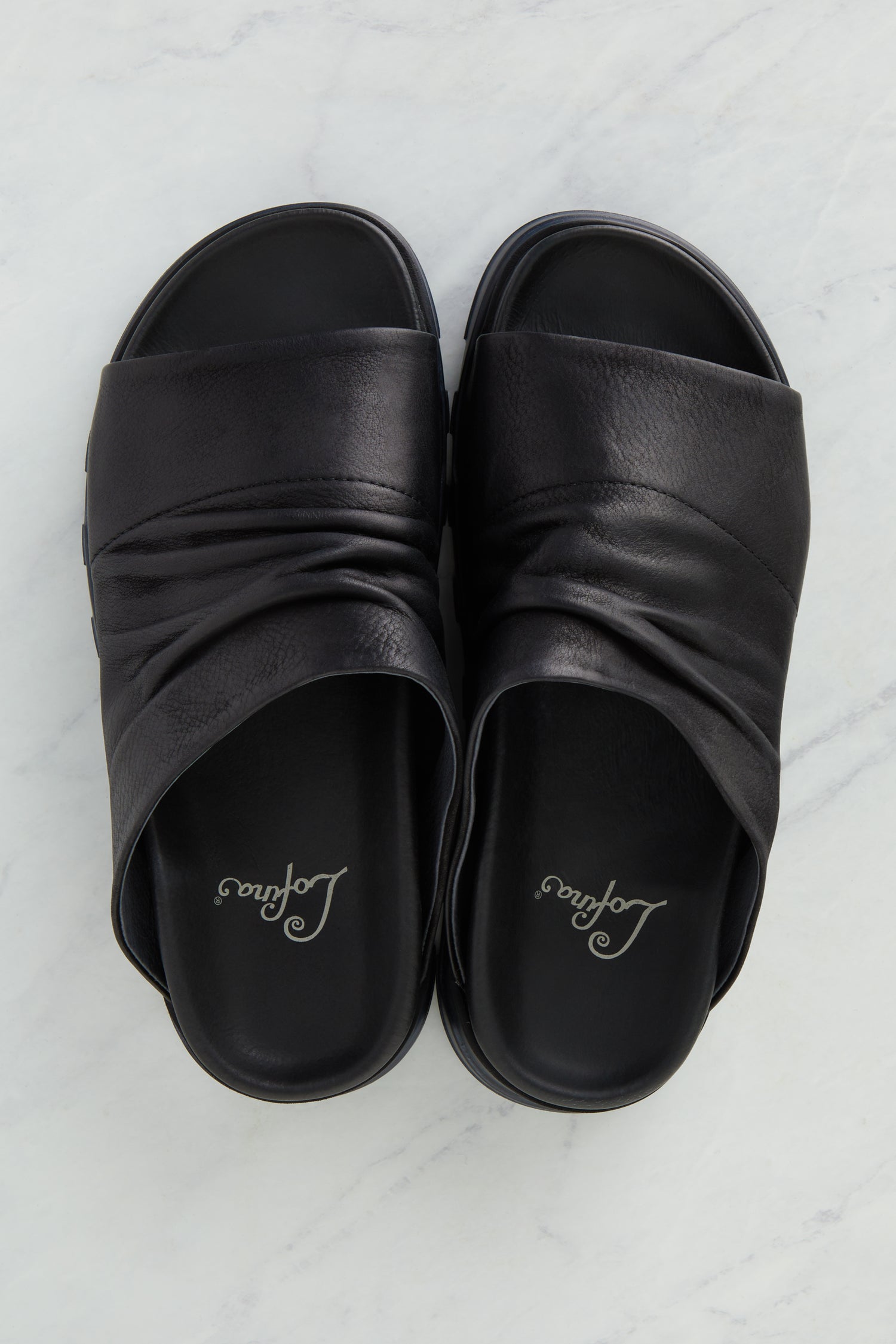 A pair of Crushed Leather Sliders crafted with handcrafted quality, displayed elegantly on a marble surface.