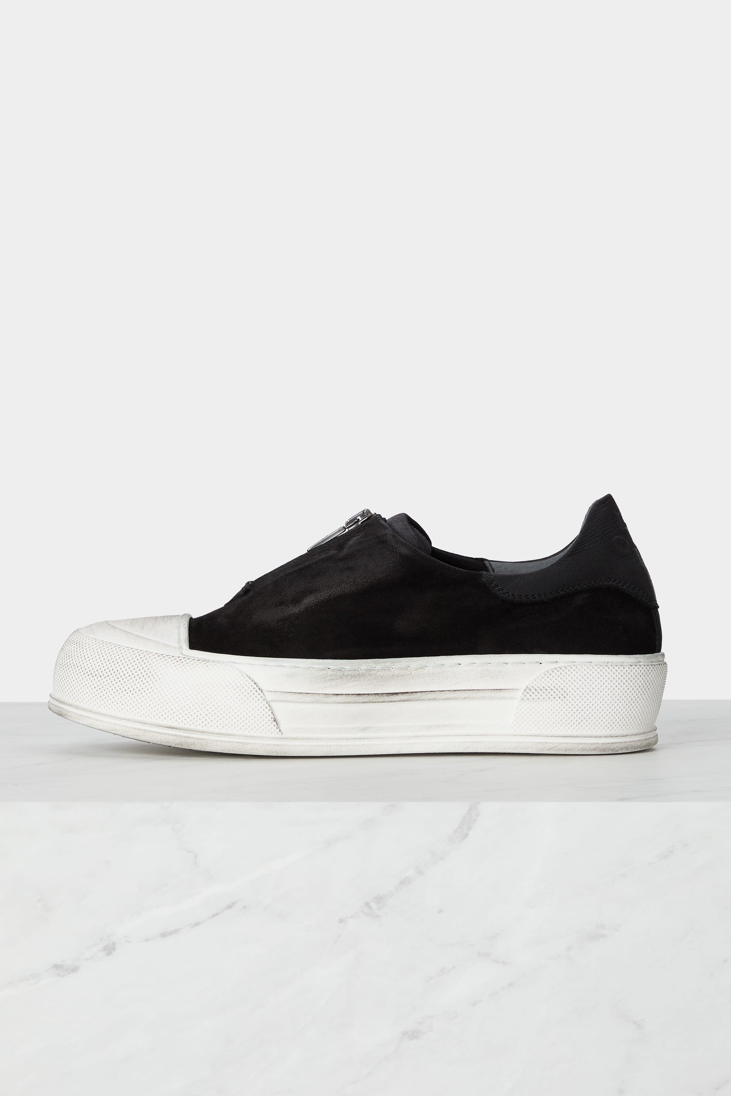 A pair of handcrafted black and white Zip Detail Suede Pumps on a minimalist marble floor.