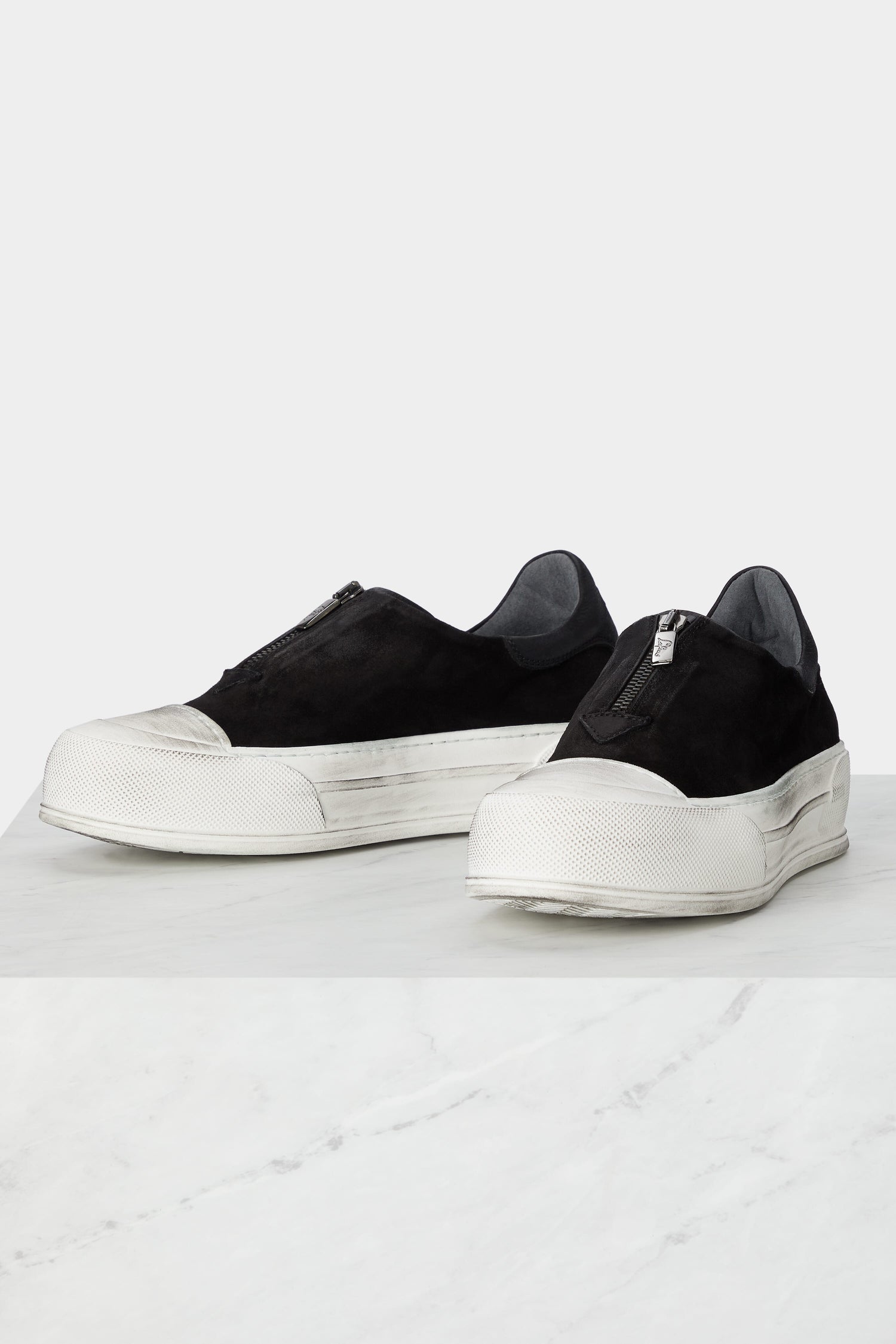 A pair of handcrafted black slip on Zip Detail Suede Pumps on a minimalist style marble table.