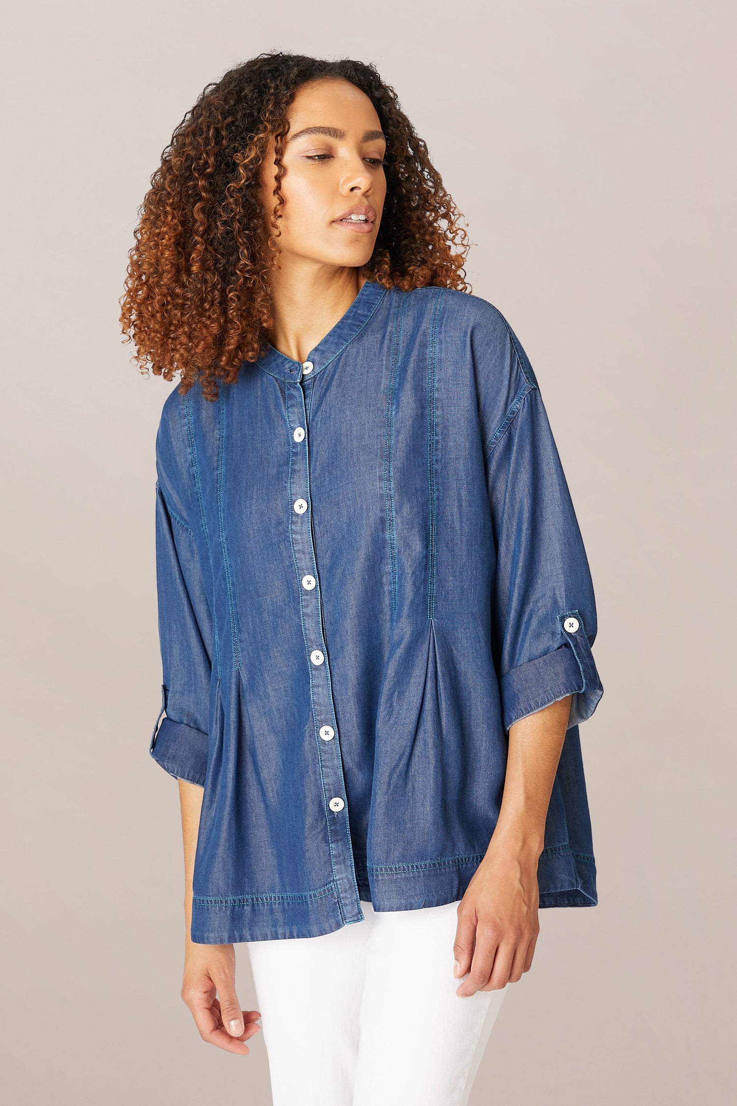 A woman in a Fluid Denim Relaxed Shirt and white pants, looking to her left with a neutral expression.