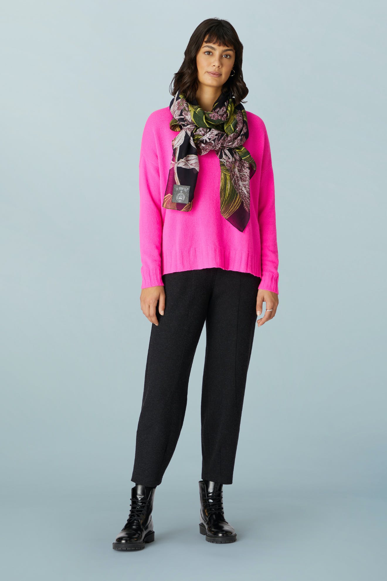 A woman wearing a bright pink sweater, a dark floral scarf, AW21 Marl Jersey Bubble Trouser, and black lace-up boots.