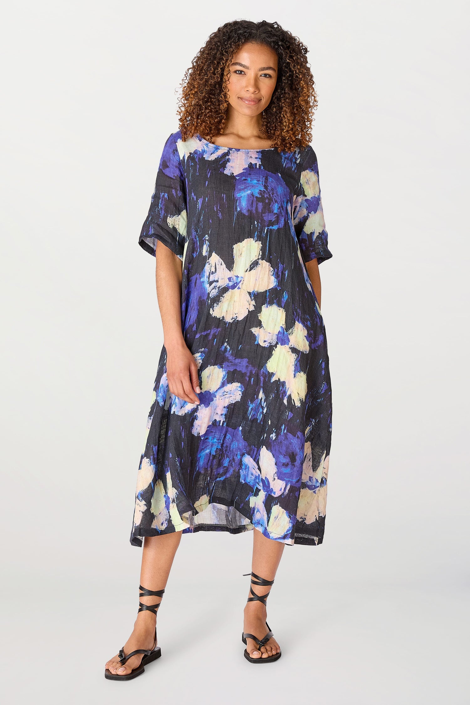 Woman in a Floral Linen Dress standing against a plain background, smiling slightly at the camera. She is wearing strappy sandals.