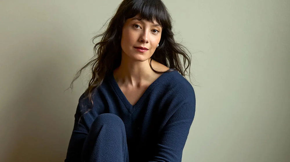 A woman with dark hair and bangs wearing a navy blue V-neck sweater.