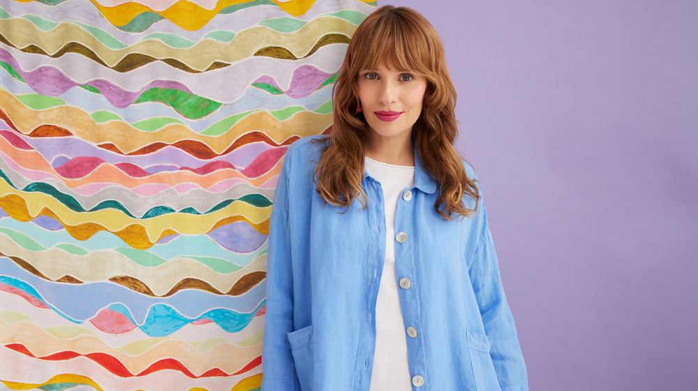 A woman in a blue jacket standing in front of a colorful wall.