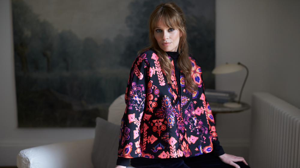 A woman is sitting in a room wearing a floral top.