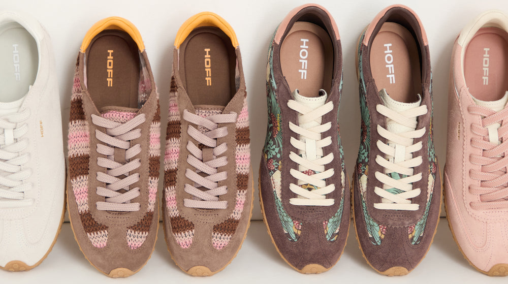 Five pairs of ankle boots in different colors and materials are lined up on a wooden floor.