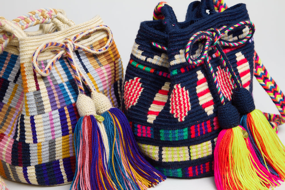 Two colorful, handwoven bags with drawstring closures and large, multicolored tassels are displayed side by side against a plain background.
