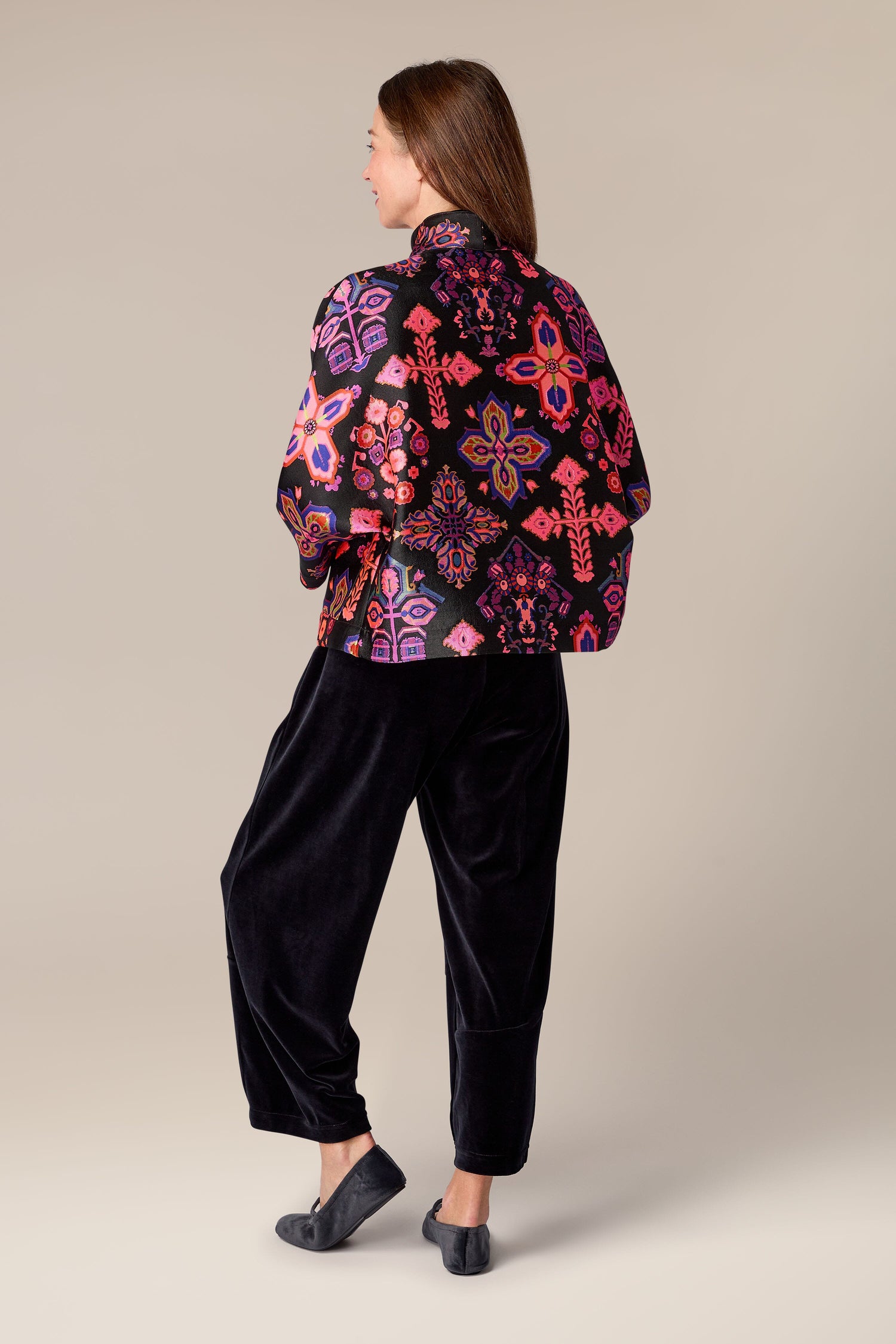 The back view of a woman wearing a Jacquard Aztec Floral Jacket and black pants.