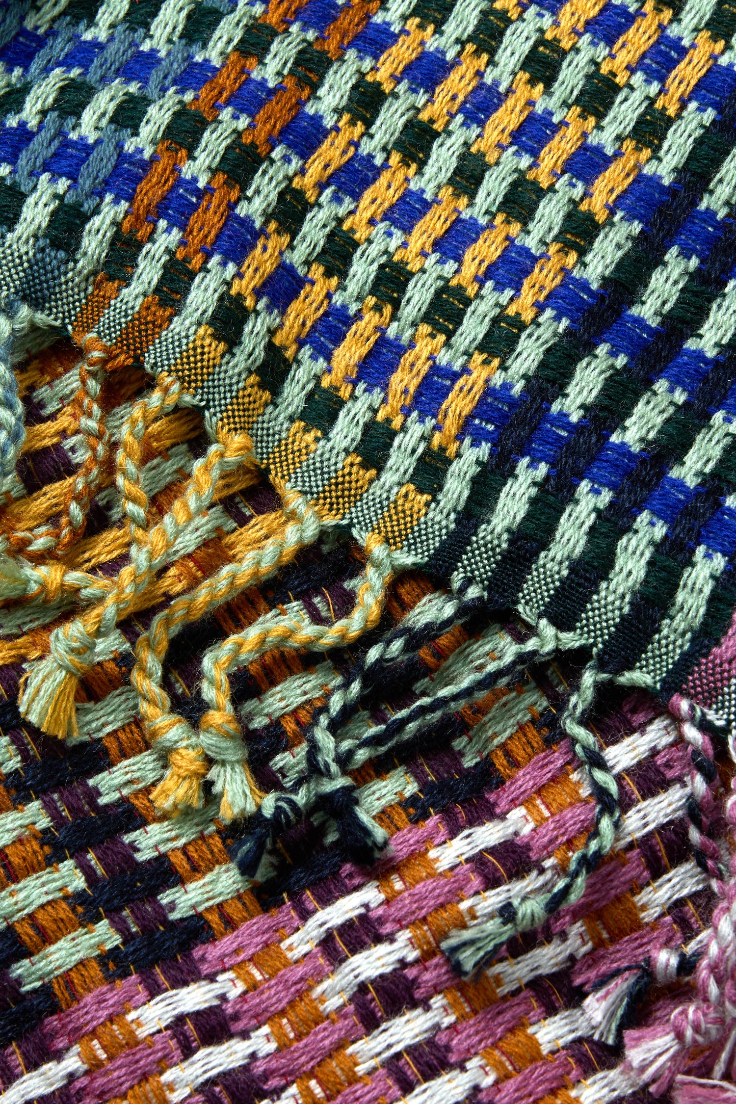 A close-up of the Woven Checkerboard Scarf, an acrylic wool blend with a blue, green, gold, and purple block pattern and knotted fringe.