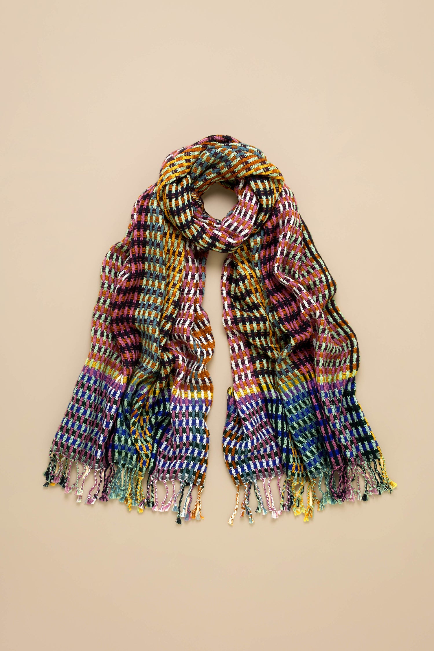 The Woven Checkerboard Scarf, made from a multicoloured acrylic wool blend with fringed ends, is laid flat on a beige background.