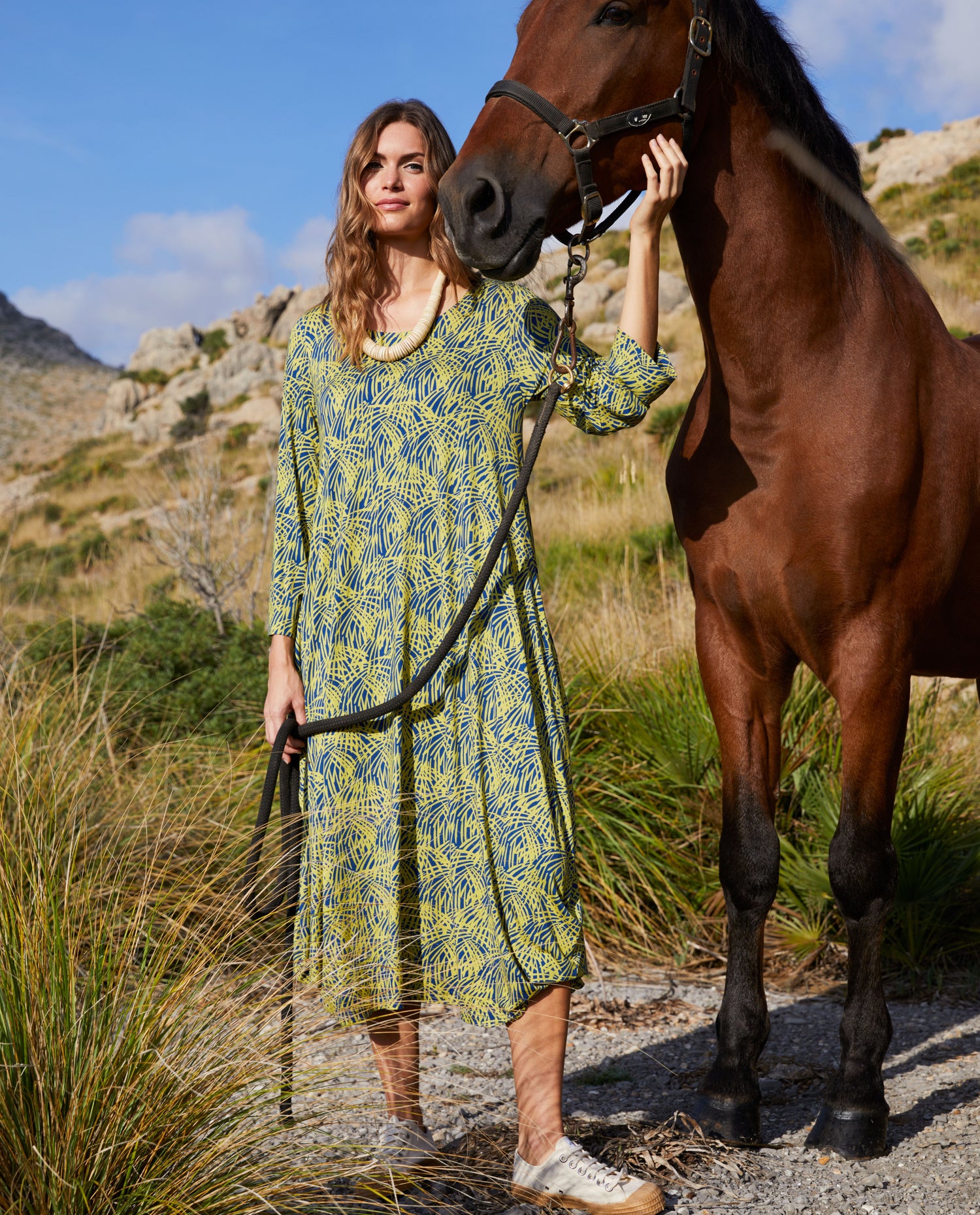 woman wearing a yellow and blue dress stood next to a horse