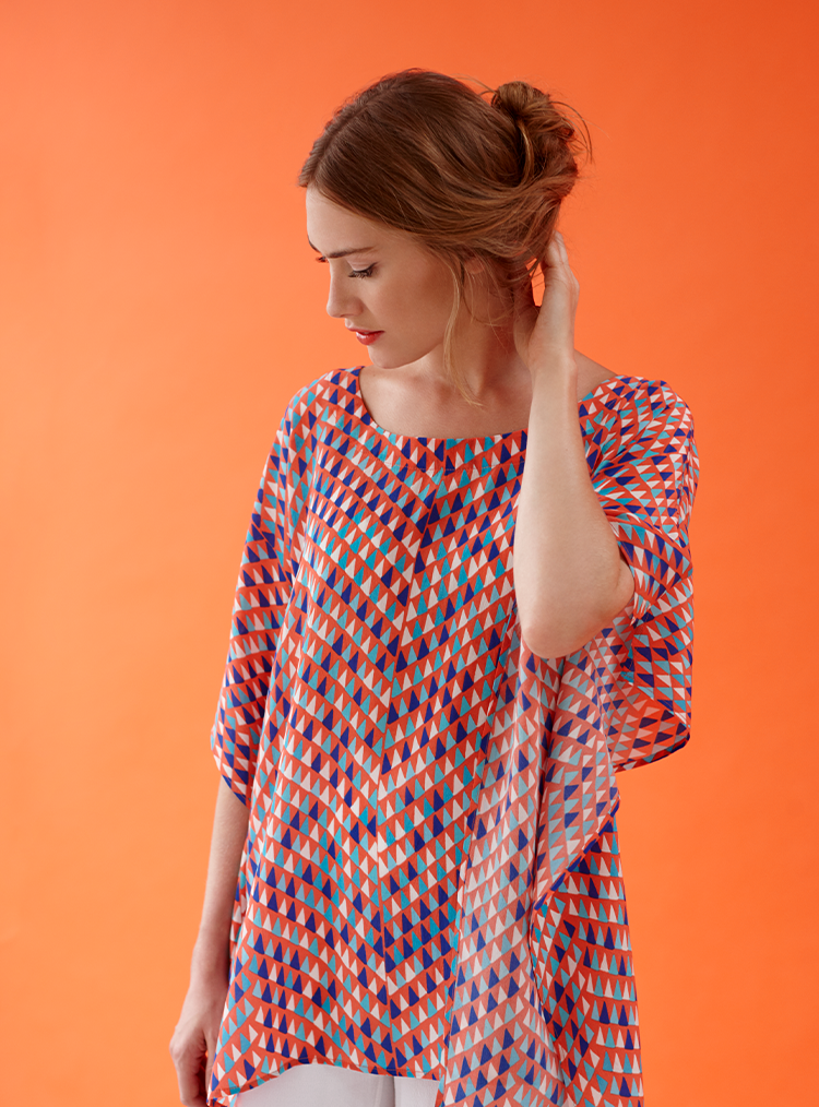 woman wearing a multi-coloured patterned top against an orange background