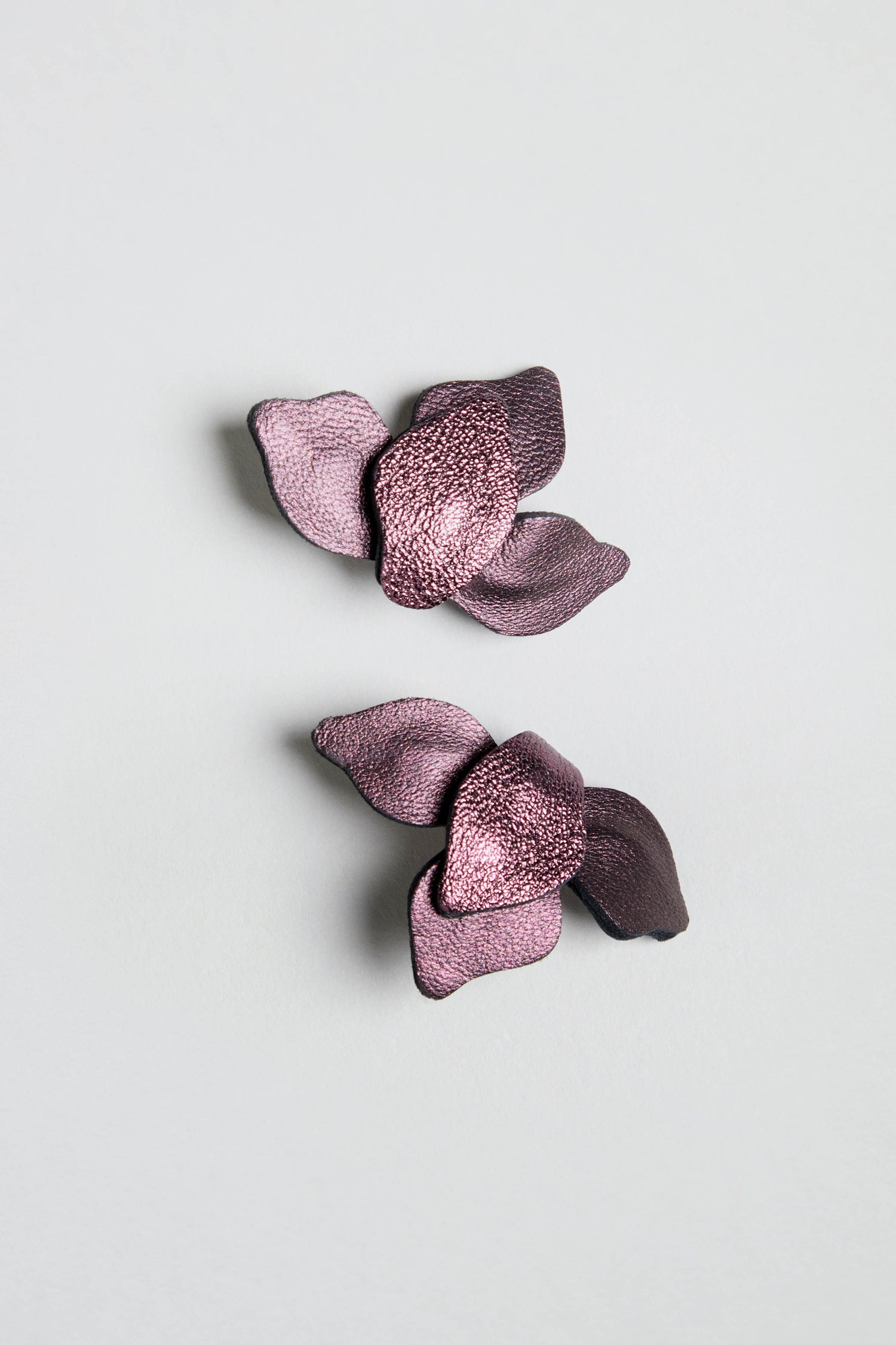 A pair of Metallic Burgundy Leather Petal Earrings are displayed on a plain light gray background.