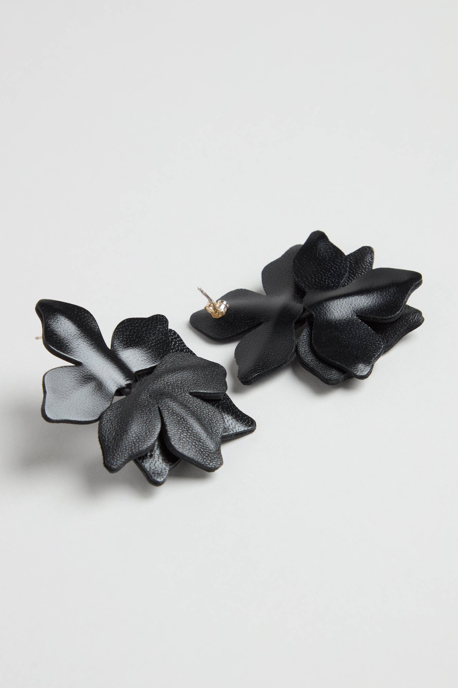 Metallic Leather Flower Earrings, featuring black layered petals in a floral design, are displayed on a plain light surface.