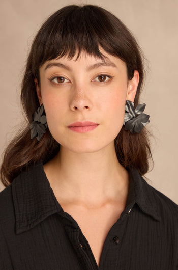 Woman with straight brown hair wears a black textured blouse and Metallic Leather Flower Earrings, posing against a neutral backdrop.