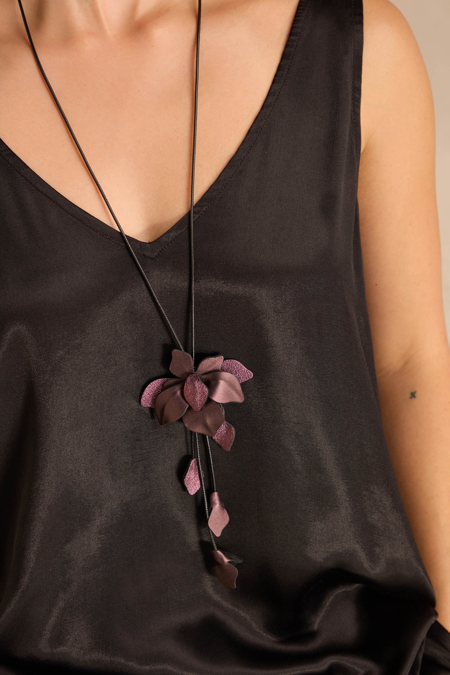 Person wearing a black satin V-neck top and the Metallic Leather Flower Necklace with a striking purple flower pendant.