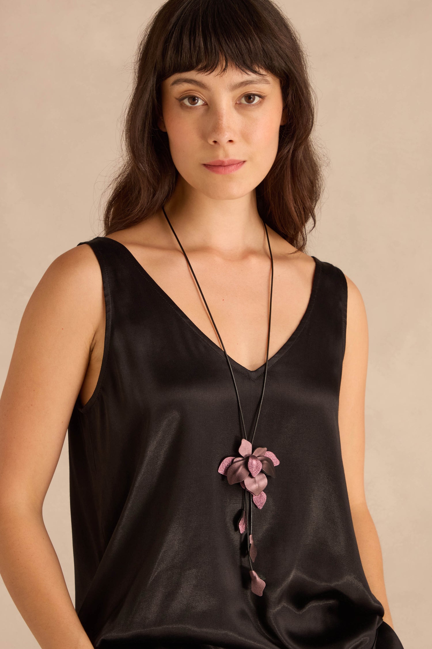 Woman wearing a black sleeveless top and the Metallic Leather Flower Necklace, featuring a large purple flower pendant, against a neutral background.