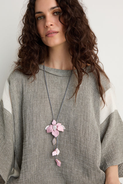 Woman with long curly hair wears a loose gray top and the Leather Flower Pendant necklace featuring a handcrafted pink leather flower, standing against a plain light background.