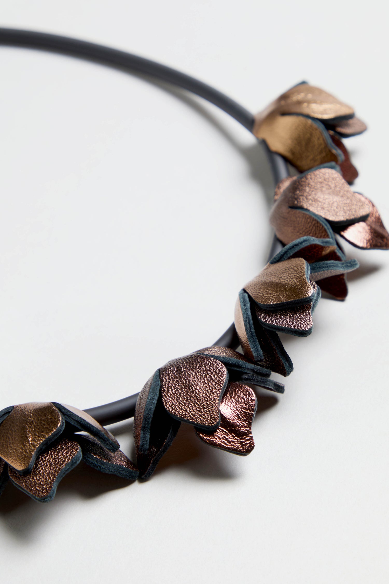 Close-up of the Short Metallic Leather Petals Necklace with bronze and copper petal-shaped elements on a black band, shown against a light background.