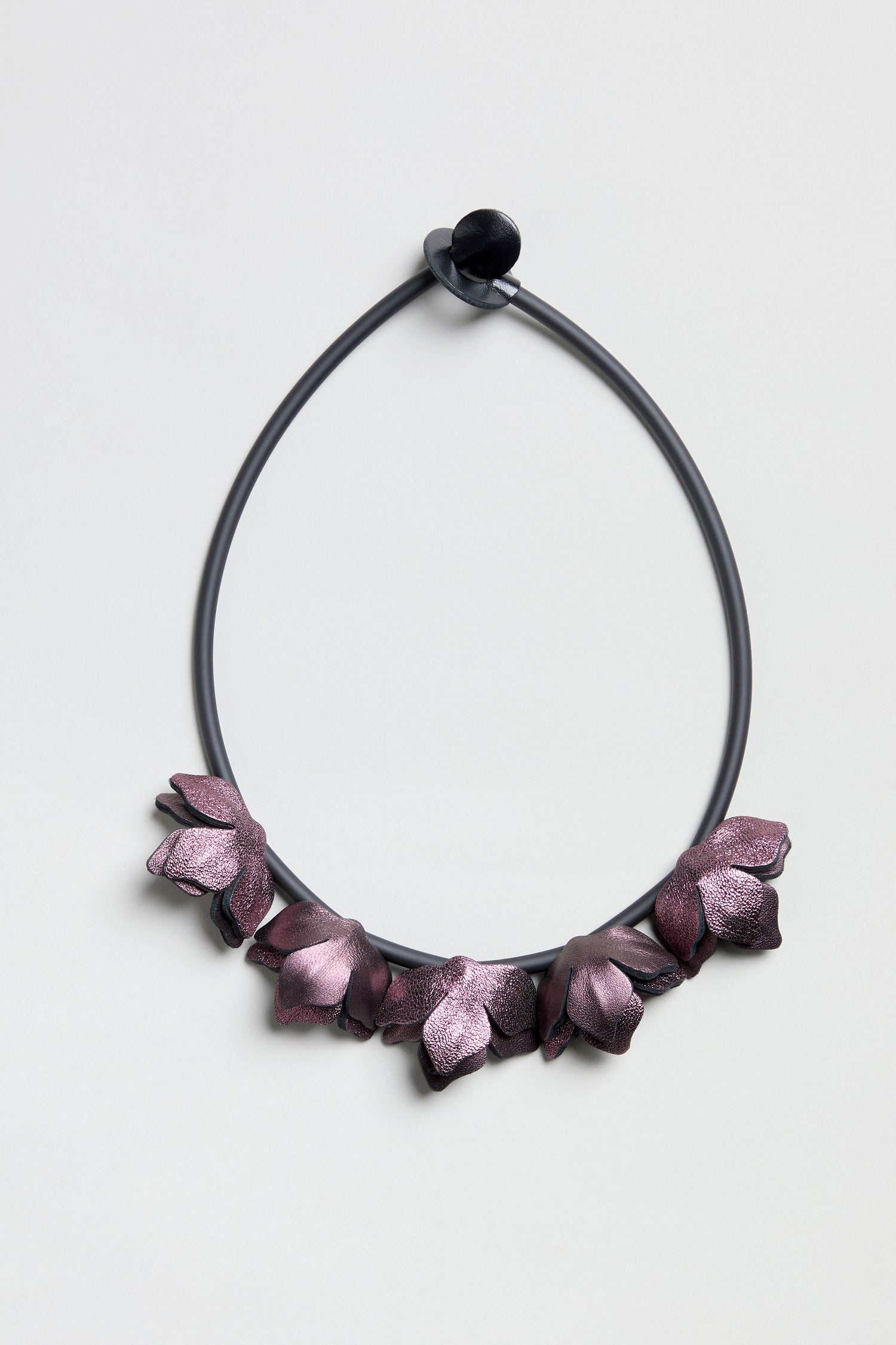 Short Metallic Leather Petals Necklace with purple flower-shaped accents on a black circular cord, shown on a light gray background.