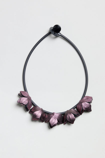 Short Metallic Leather Petals Necklace with purple flower-shaped accents on a black circular cord, shown on a light gray background.