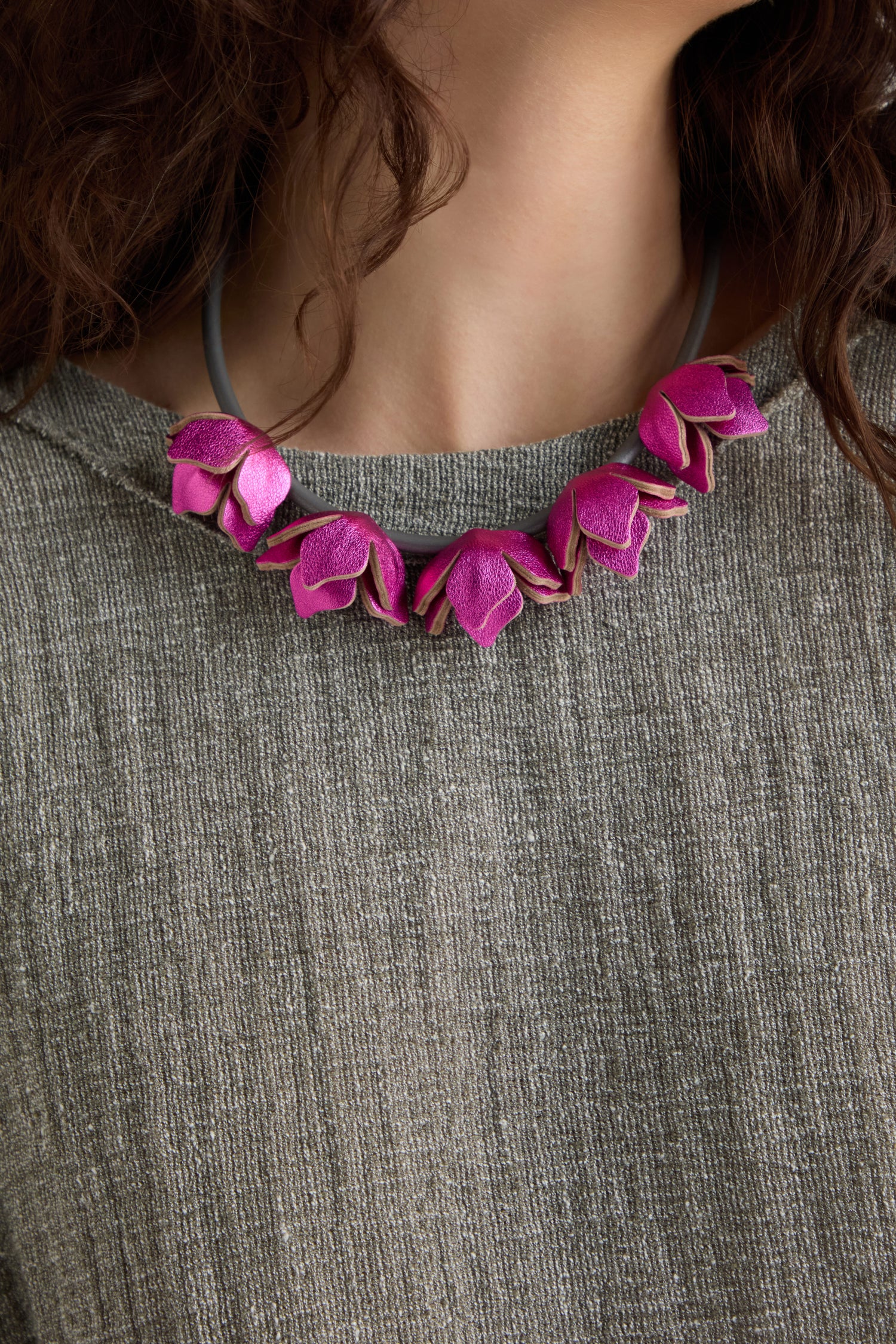 Person wearing a gray textured top and the Short Leather Petals Necklace, featuring metallic fuchsia tones and pink flower-shaped beads.