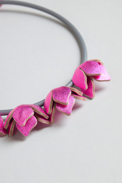 The Short Leather Petals Necklace features several metallic pink petal-shaped charms and is displayed on a light background, adding a chic touch to any look.