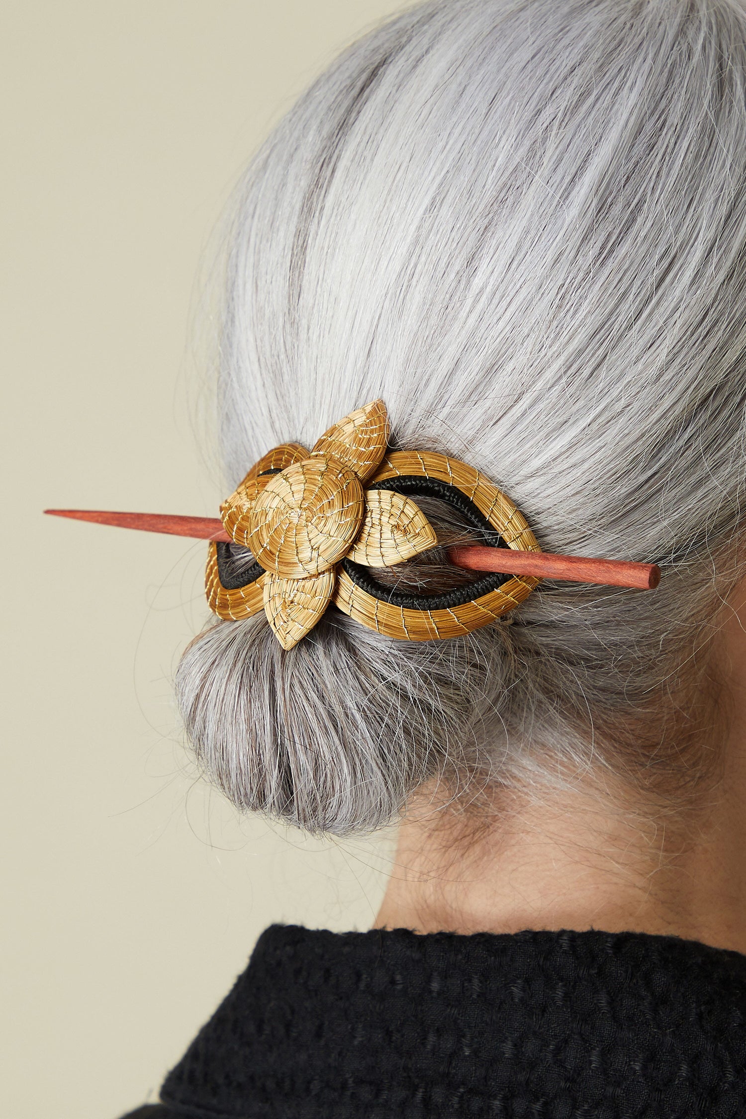 A person with silver hair styled in a bun, secured by a Golden Grass Woven Flower Hair Pin featuring a natural flower hair accessory.