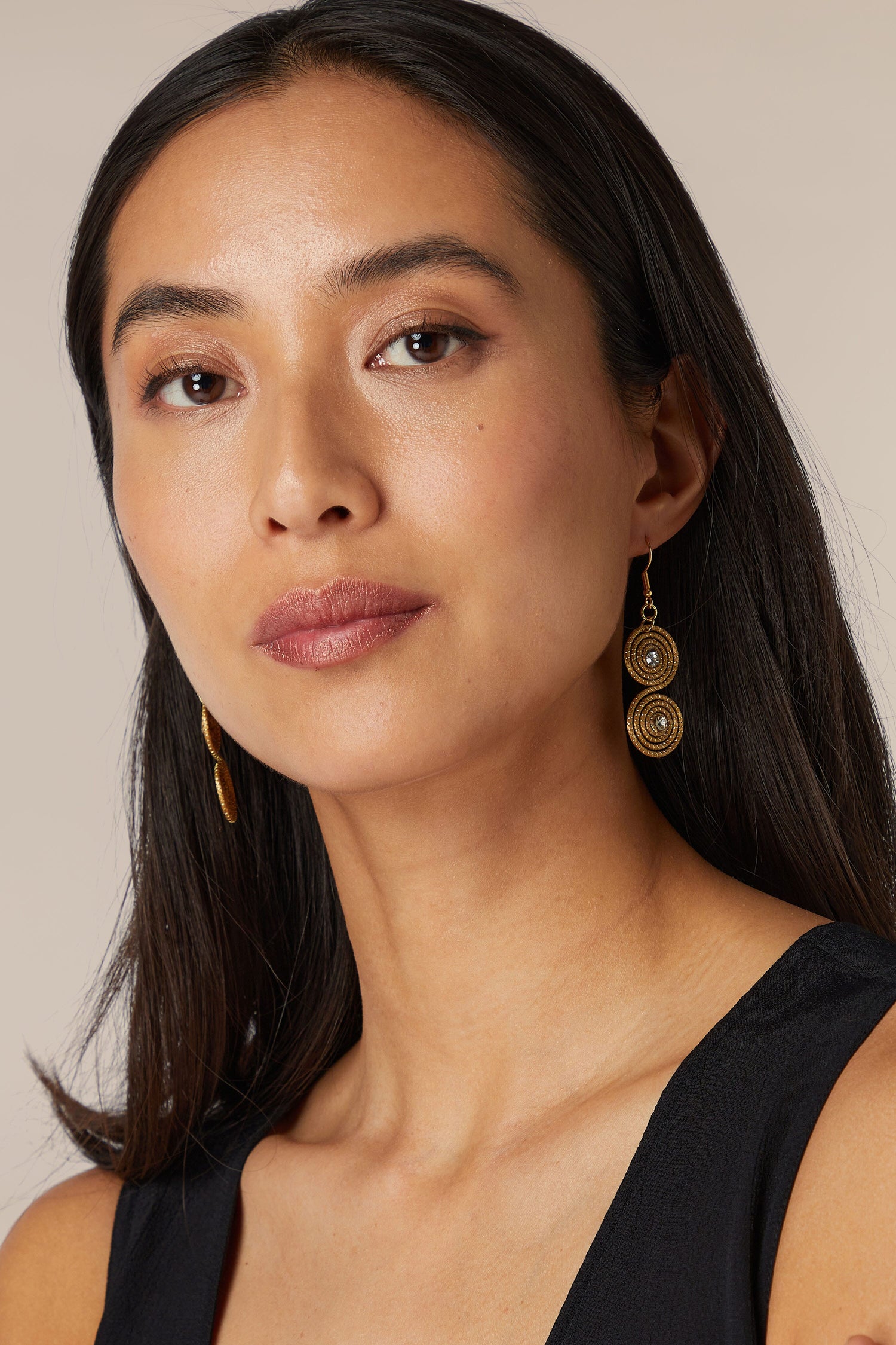 A woman wearing Golden Grass Spiral Rhinestone Earrings and a black top poses for a portrait with a neutral expression.