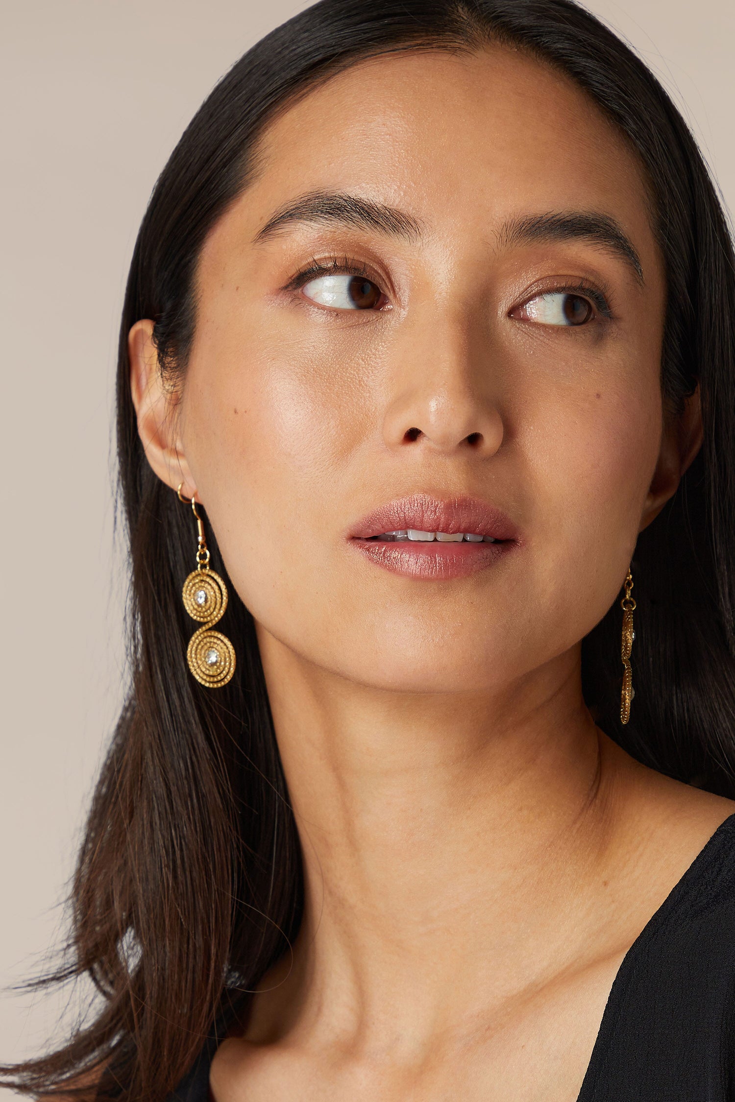 A woman with dark hair wearing Golden Grass Spiral Rhinestone Earrings and looking away from the camera.