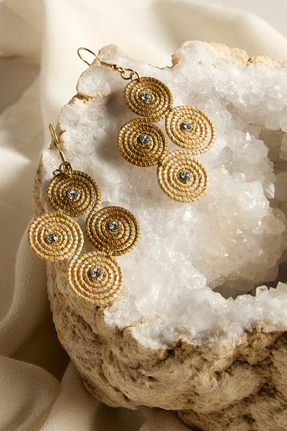 The Golden Grass Woven Spiral Rhinestone Earrings are elegantly showcased on a crystal geode and light fabric, capturing the essence of sustainable jewelry.