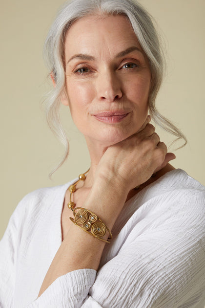 An elegant senior woman with silver hair wearing a white blouse and a Golden Glass Spiral Rhinestone Bracelet.