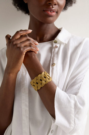 A person in a white shirt clasps their hands, adorned with the artisanal Golden Grass Woven Bracelet.