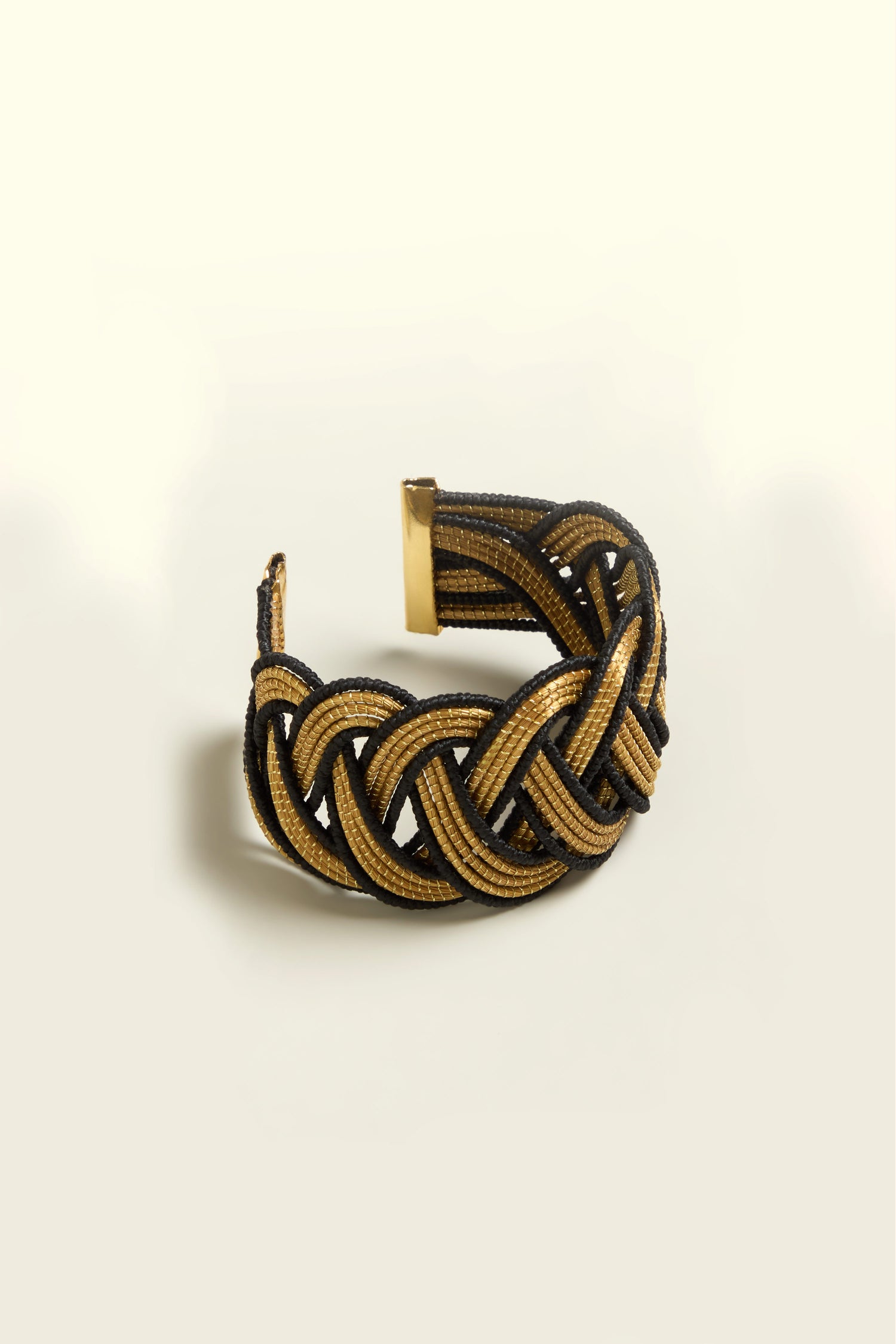 The Gold and Black Grass Woven Bracelet, with its intertwined strands and clasp closure, is displayed elegantly on a neutral background.