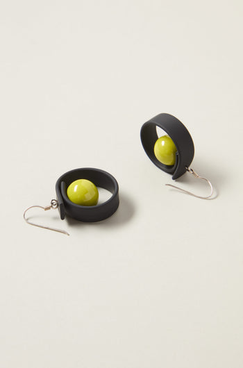 The Tempo Earrings feature black circular band designs with green spheres at the center, crafted from durable materials and featuring hook clasps; a fine example of modernist French jewelry.