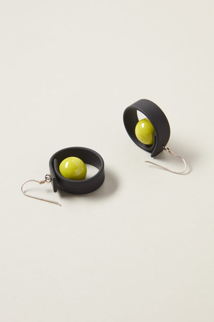 The Tempo Earrings feature black circular band designs with green spheres at the center, crafted from durable materials and featuring hook clasps; a fine example of modernist French jewelry.