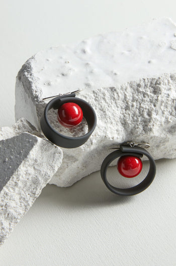 A pair of Tempo Earrings in black and red, crafted through jewellery making. The earrings are delicately placed on a rock, showcasing their fabrication expertise.