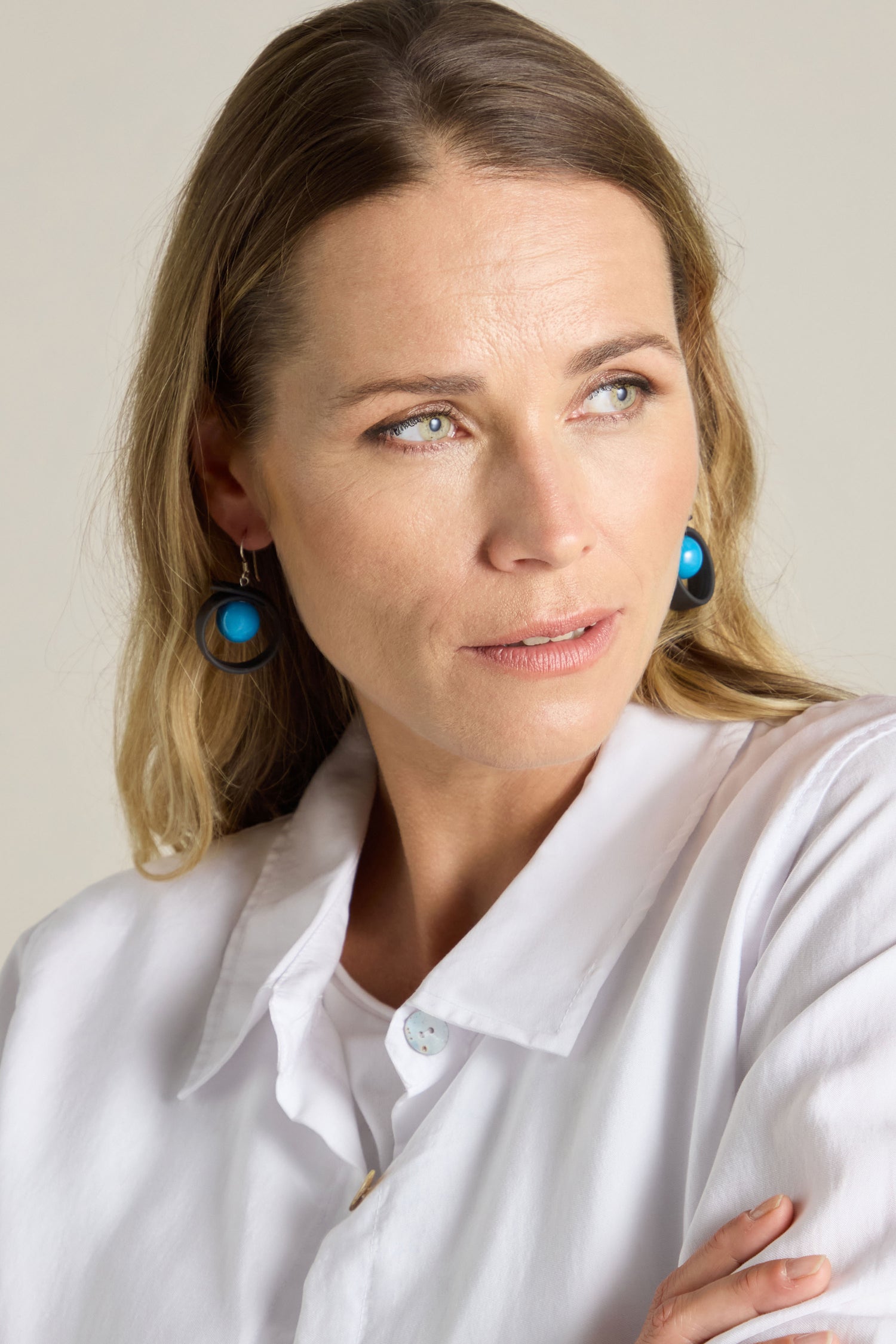 A person with light hair wearing a white shirt and blue Tempo Earrings, designed for durability, glances to the side with a neutral expression.