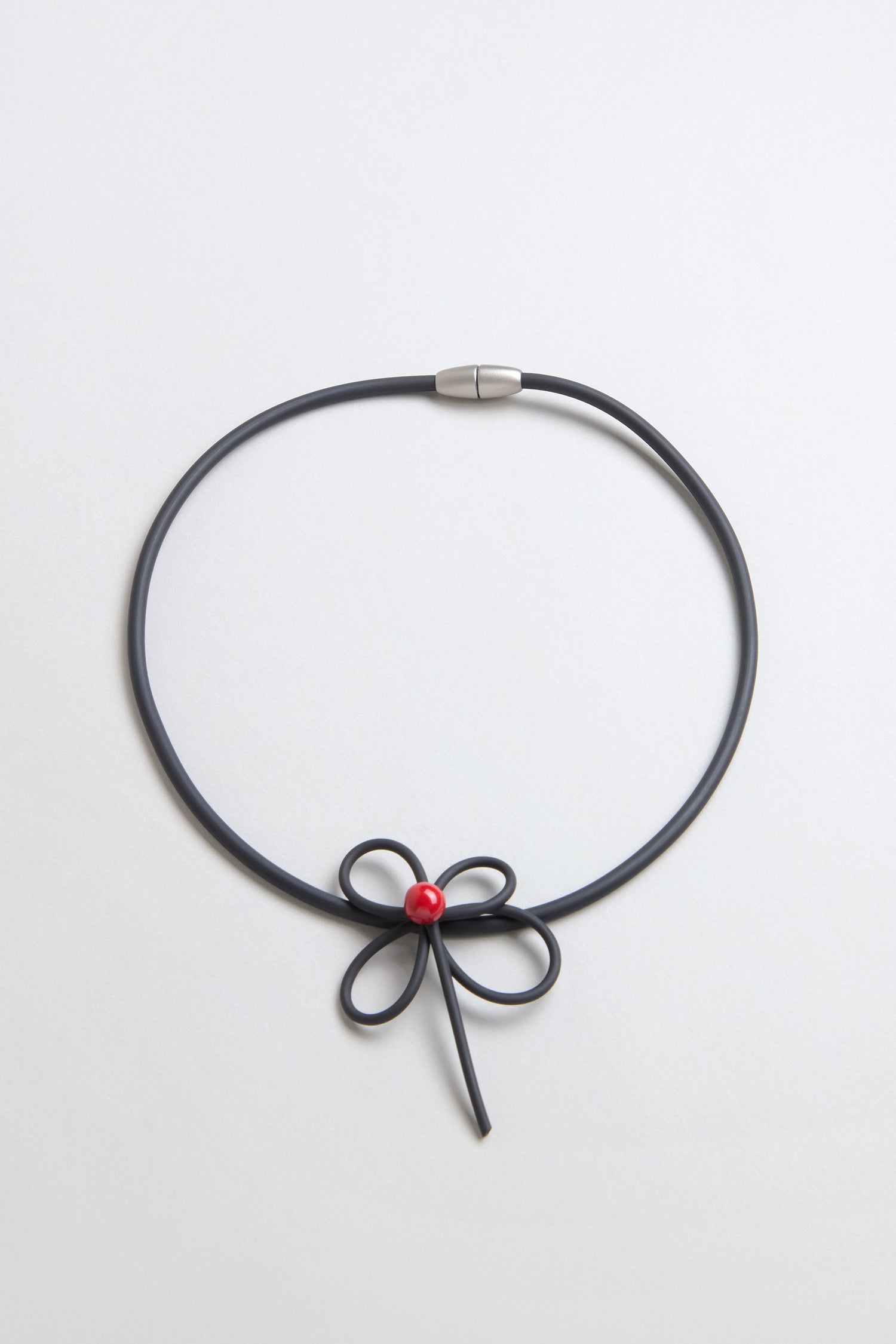 The Flower Necklace features a bow-shaped center with a single red bead, reminiscent of handmade ceramic jewelry, displayed against a plain light background.