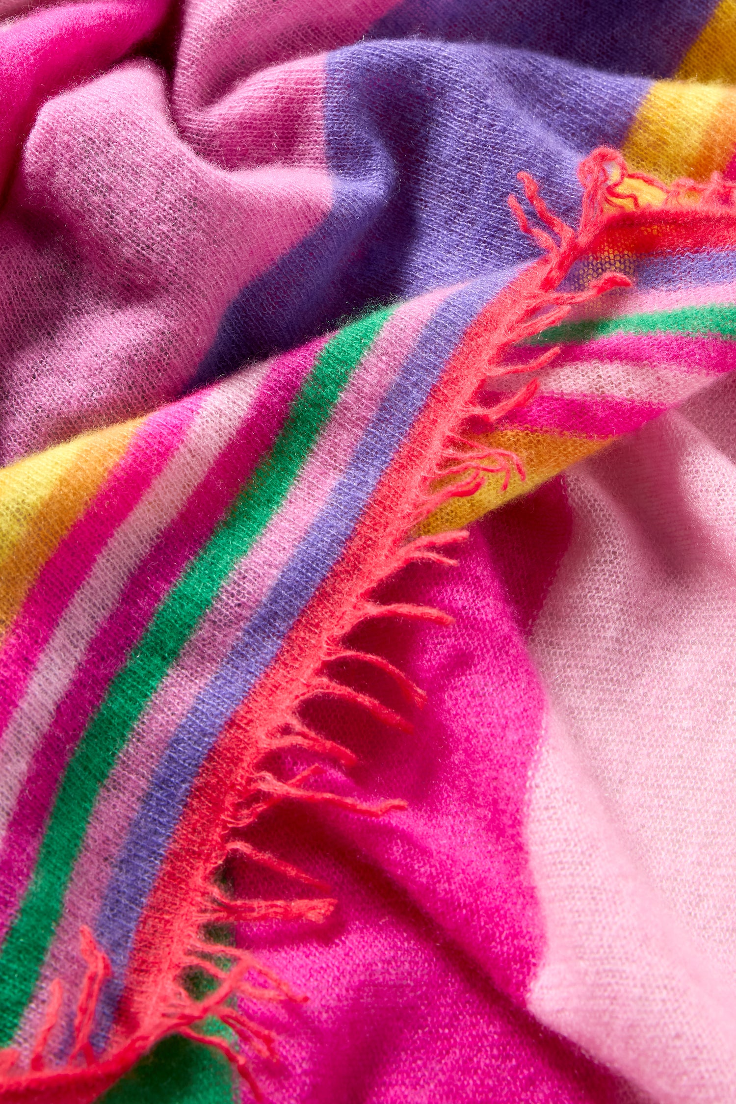 A close-up of the Colour Pop Stripe Cashmere Scarf highlights its soft fabric with pink, purple, yellow, and green stripes and frayed red threads along one edge.
