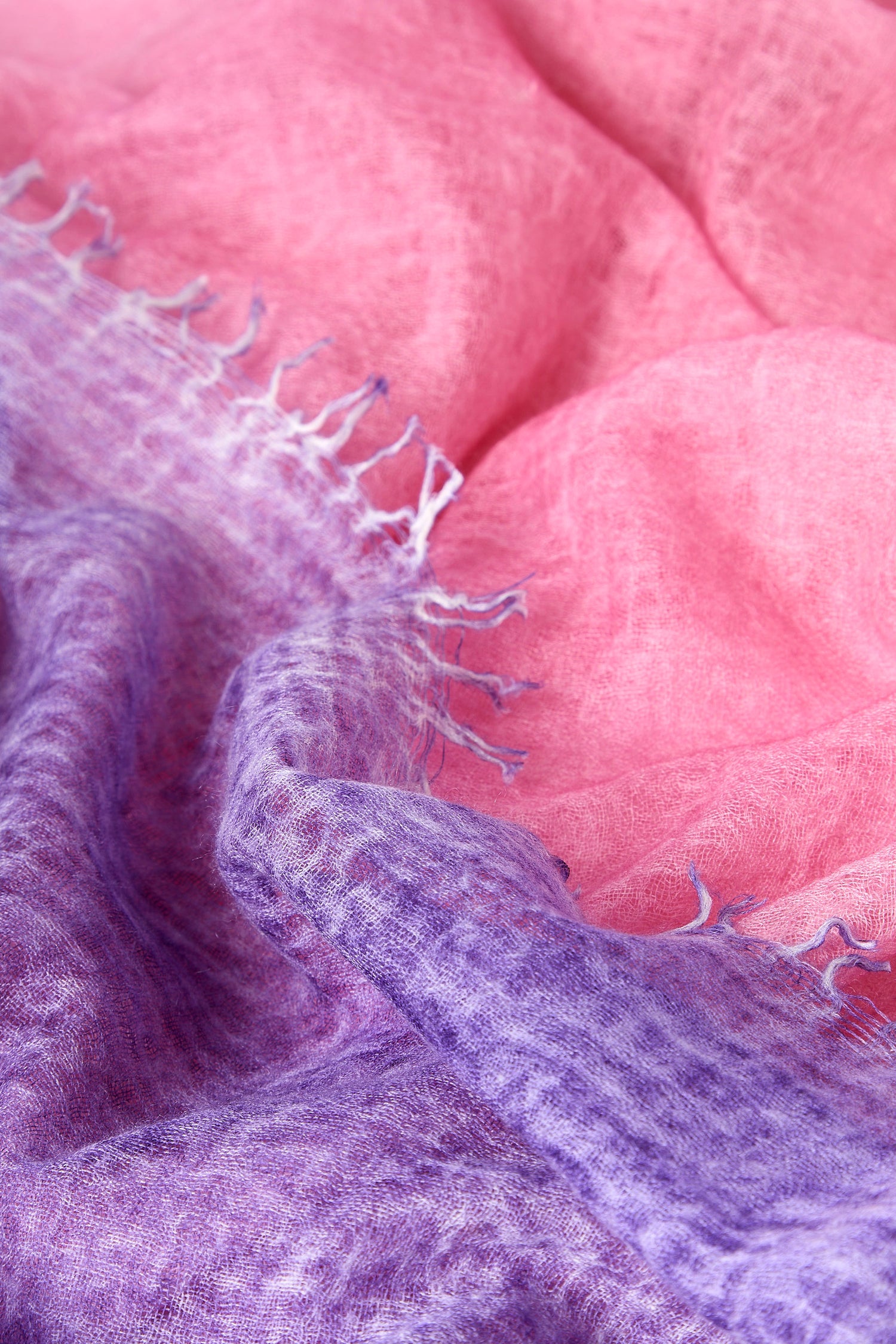 A close-up of the Harmony Cashmere Scarf reveals crinkled fabric in pink and purple shades, showcasing textured fibers and fringed edges, reminiscent of a cozy, multi-tonal accessory perfect for Autumn.