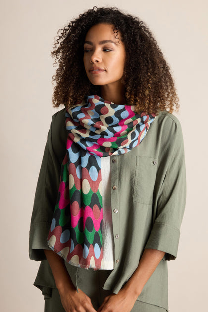 A person wearing a green shirt and a Retro Waves Wool Mix Scarf with a pattern of overlapping circles in various colors, exuding a vintage style.