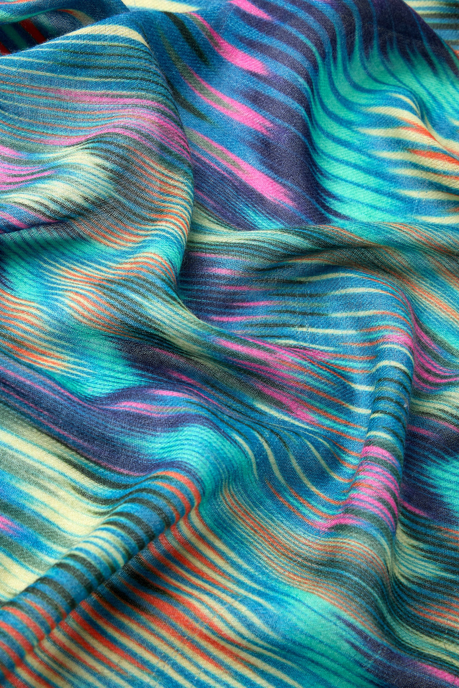 Close-up of a vibrant Autumnal Ikat Wool Scarf showcasing colorful, striped fabric with a wavy texture. The scarf features brilliant hues of blue, green, pink, yellow, and orange, reminiscent of an ikat inspired print.