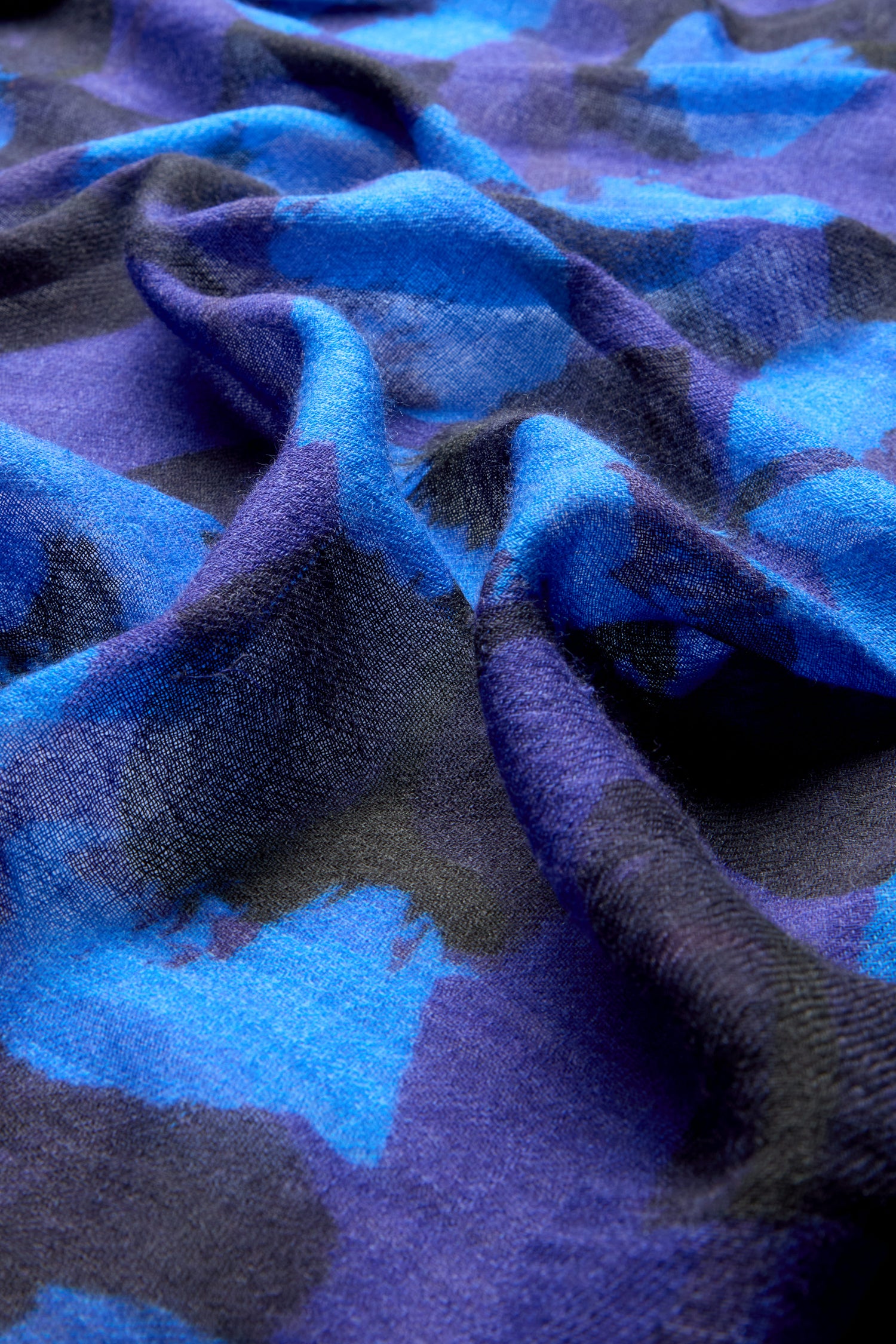 Close-up of the Flowering Poppies Wool Scarf showcasing its soft, smooth texture with a dark blue and black abstract pattern. The luxurious material appears slightly ruffled and draped—perfect for a winter wardrobe upgrade.