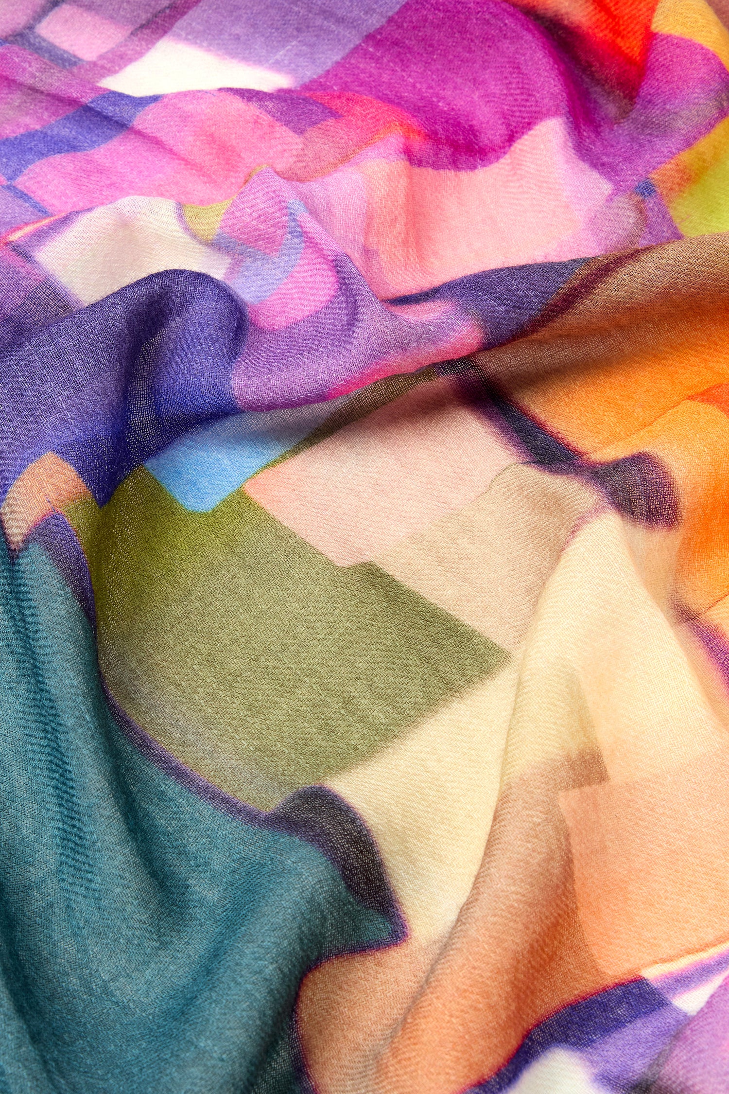 A close-up image of fabric featuring a vibrant, multicolored geometric pattern with soft folds and a smooth texture, reminiscent of the premium Square Collage Wool Scarf.