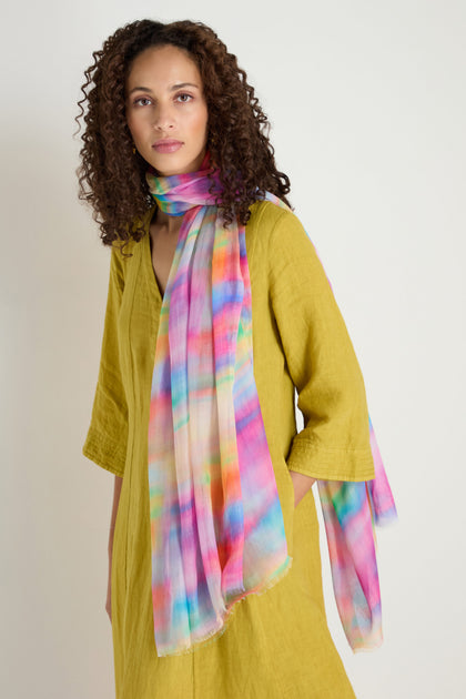 A woman in a mustard yellow dress stands against a light background, her vibrant look complemented by the lightweight Painted Horizon Scarf in modal and silk, adding an elegant touch.