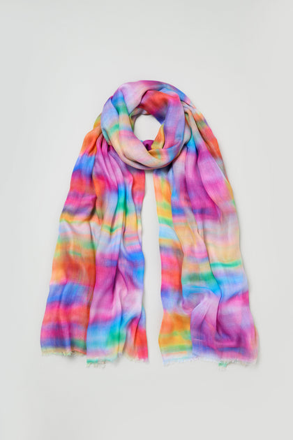 The Painted Horizon Scarf is a lightweight accessory made from luxurious modal and silk, featuring a soft, multicolored rainbow pattern, shown laid flat on a white background.
